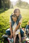 Щаслива молода мати з милою маленькою донькою в подібному одязі насолоджується сонячним літнім днем разом, сидячи на ковдрі на трав'янистій галявині в парку — стокове фото