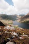 Vue arrière de la femelle anonyme admirant les collines et la rivière tout en étant assis sur une pente rugueuse pendant le voyage à travers Snowdonia, campagne britannique — Photo de stock