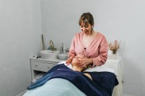 Content masseuse massaging shoulders of female client lying on table in beauty salon — Stock Photo