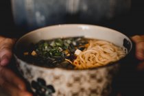 Chinese ramen meal in ceramic bowl with oriental ornament placed on wooden table on black background — Stock Photo