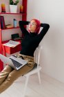 Freelancer jovem focado em roupas casuais sentado na cadeira olhando para longe usando laptop enquanto trabalhava no projeto em luz apartamento moderno — Fotografia de Stock