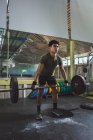 Сосредоточенный азиатский спортсмен делает тягу с тяжелой штангой во время тренировки в спортзале, отводя взгляд — стоковое фото