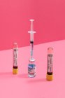 Coronavirus negativer und positiver Bluttest in der Nähe von Impfflasche und Spritze auf rosa Hintergrund — Stockfoto