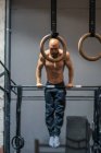 Ganzkörperhemdloser bärtiger Sportler hängt an der Stange und macht Klimmzüge während des intensiven Trainings im modernen Fitnessstudio — Stockfoto