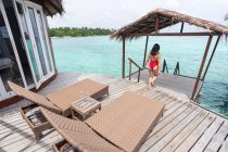 Vue arrière de la femelle anonyme en maillot de bain descendant les escaliers dans l'eau relaxant aux Maldives — Photo de stock