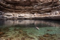 Donna anonima rilassata galleggiante sull'acqua trasparente di Bimmah Sinkhole circondata da rocce grezze durante il viaggio in Oman — Foto stock
