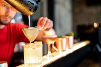 Barista concentrato versando cocktail rinfrescante freddo attraverso colino in vetro posto sul bancone in bar — Foto stock