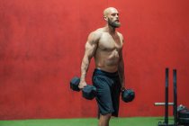 Side view of strong bearded athlete looking away with heavy dumbbells walking in modern gym during weightlifting workout — Stock Photo