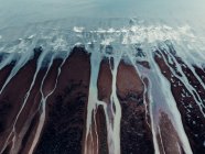 Desde arriba paisaje texturizado aéreo de áspera costa pedregosa desigual y espumosas olas oceánicas con arroyos - foto de stock