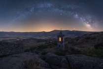 Increíble paisaje con capilla de piedra envejecida en el valle montañoso bajo el cielo nocturno con la Vía Láctea y la luz del atardecer - foto de stock