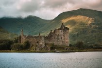 Damaged old castle located on coast of calm lake against grassy hills on the countryside on cloudy day in kilchurn castle, United Kingdom — Stock Photo