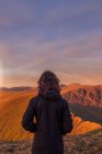 Vue arrière du randonneur anonyme debout sur une colline rocheuse dans les hautes terres et bénéficiant d'une vue sur la crête de montagne au coucher du soleil au Pays de Galles — Photo de stock