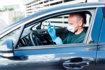 Side view of serious man using a protective mask putting on gloves driving car during quarantine time — Stock Photo