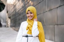Baixo ângulo de fêmea muçulmana na moda em hijab amarelo em pé na rua e olhando para longe — Fotografia de Stock