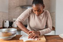 Joven mujer afroamericana aplastando plátano fresco en la tabla de cortar mientras prepara patacones en casa - foto de stock