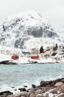 Mar frio com água tranquila localizada perto do assentamento costeiro e cume de montanha nevada no dia de inverno nublado nas Ilhas Lofoten, Noruega — Fotografia de Stock