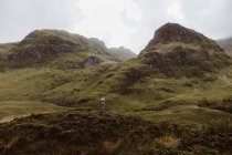 Back view of unrecognizable man standing on rough grassy hillside during trip through Glencoe in the UK countryside on cloudy day — Stock Photo