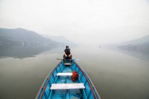Esploratore maschio galleggiante in barca di legno blu sul lago calmo nella mattina nebbiosa durante le vacanze in Nepal — Foto stock