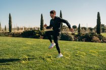 Vista laterale dell'atleta in forma maschile in abbigliamento sportivo che salta sul prato durante l'allenamento sotto il cielo blu — Foto stock