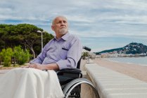 Homme âgé en fauteuil roulant sur la promenade regardant loin dans la contemplation et profitant de la vue sur la mer — Photo de stock