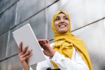 Lächelnde muslimische Unternehmerin im gelben Hijab steht auf der Straße und blättert in Tablets — Stockfoto