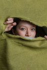 Junge grünäugige Frau blickt in die Kamera, während sie sich hinter zerrissenem grünem Tuch versteckt — Stockfoto