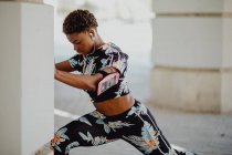 Молодая фитнесс афроамериканка растягивает ноги перед бегом по городской улице — стоковое фото