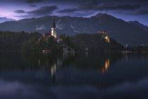 Espectacular paisaje de estanque tranquilo con isla y castillo situado en las tierras altas rocosas de Eslovenia durante la puesta del sol - foto de stock