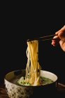 Mano di donna che tiene bacchette di bambù con gustose tagliatelle di grano dal piatto di farina di ramen cinese — Foto stock