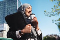 Снизу веселые мусульманские предпринимательницы в хиджабе и с кофе на вынос, стоящим на улице — стоковое фото