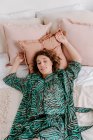 Hohe Winkel der ruhigen Frau in häuslicher Kleidung ruht auf weichem Bett zu Hause und blickt in die Kamera — Stockfoto