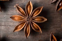 Closeup of aromatic dried anise stars with seeds scattered on rustic wooden table for gastronomy concept background — Stock Photo