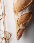 Zusammensetzung von köstlichen frisch gebackenen rustikalen Baguette auf weißer Oberfläche mit getrockneten Weizenspikes — Stockfoto