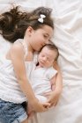 Vista superior de la niña alegre abrazando bebé adorable mientras está acostado en la cama suave en casa - foto de stock