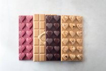 Dall'alto di deliziose barrette di cioccolato colorate poste in fila su sfondo bianco — Foto stock