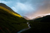 Ciel couvert au coucher du soleil sur la pente de la colline et la rivière courbée dans la soirée paisible à Glen Etive, Royaume-Uni — Photo de stock