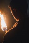 Вид сзади на обрезанный анонимный спелеолог-мужчина с пылающим факелом, стоящим в темно-узкой скалистой пещере, исследуя подземную среду — стоковое фото