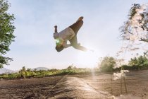 Masculino acrobático saltando sobre el suelo y realizando un peligroso truco de parkour en un día soleado - foto de stock