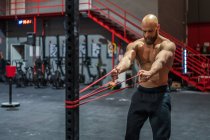 Muskulöser bärtiger Mann zieht beim funktionellen Training im modernen Fitnessstudio mit Mühe ein elastisches Seil — Stockfoto