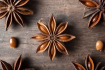 Крупный план ароматических сушеных анисовых звезд с семенами, разбросанными по деревенскому деревянному столу для гастрономии — стоковое фото