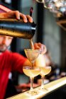 Focado cortado bartender irreconhecível derramando cocktail refrescante frio através de coador em vidro colocado no balcão no bar — Fotografia de Stock