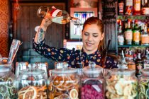 Barkeeperin gießt Alkohol in Shaker, während sie am Tresen in der Bar einen erfrischenden Cocktail zubereitet und wegschaut — Stockfoto