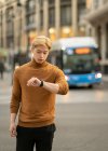 Ernsthafter ethnischer Mann kontrolliert Zeit auf Armbanduhr, während er auf der Straße steht und auf ein Treffen wartet — Stockfoto