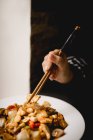 Unerkennbares Weibchen mit Essstäbchen isst Portion leckeres Gong Bao Huhn vor schwarzem Hintergrund im Restaurant — Stockfoto