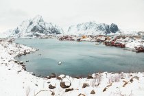 Холодне море з тихою водою, розташованою біля прибережного поселення та снігового гірського кряжа в день зимівлі на Лофотенських островах (Норвегія). — стокове фото