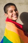 Contenuto giovane donna etnica bisessuale con bandiera multicolore che rappresenta i simboli LGBTQ guardando la fotocamera nella giornata di sole — Foto stock