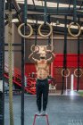 Full length strong shirtless man standing on stool and preparing to do exercise on gymnastic rings during intense workout in modern gym — Stock Photo