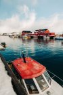Desde arriba moderno barco a motor flotando en el agua de mar cerca de muelle nevado en pacífico asentamiento costero con casas rojas en el día nublado de invierno en las Islas Lofoten, Noruega - foto de stock