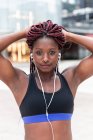 Ethnic muscular African American sportswoman holding braids and looking at camera on street — Stock Photo