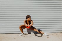 Jeune femme afro-américaine fitness étirant les jambes avant de courir dans la rue de la ville — Photo de stock